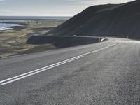 a car on a highway near the ocean and grassy area with water and hills in the background