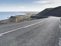 a car on a highway near the ocean and grassy area with water and hills in the background