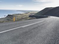 a car on a highway near the ocean and grassy area with water and hills in the background