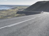 a car on a highway near the ocean and grassy area with water and hills in the background