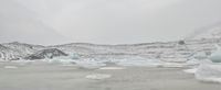 large number of ice pieces on the ground by water with snow covering it and mountains