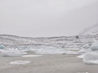 large number of ice pieces on the ground by water with snow covering it and mountains