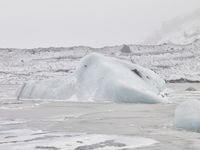 large number of ice pieces on the ground by water with snow covering it and mountains