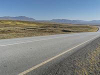 a road with a yellow line and mountains in the background and there is a bicycle resting next to the curve