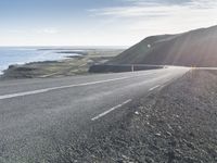 an empty road with a couple cars on it at the side of it and some hills