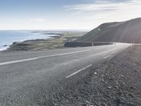 an empty road with a couple cars on it at the side of it and some hills