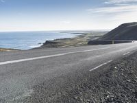 an empty road with a couple cars on it at the side of it and some hills