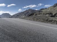 a motorcycle on the road surrounded by mountains and clouds in front of it, while someone is riding on one side of the lane