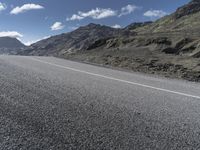 a motorcycle on the road surrounded by mountains and clouds in front of it, while someone is riding on one side of the lane