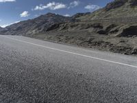 a motorcycle on the road surrounded by mountains and clouds in front of it, while someone is riding on one side of the lane