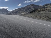 a motorcycle on the road surrounded by mountains and clouds in front of it, while someone is riding on one side of the lane