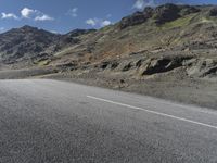 a motorcycle on the road surrounded by mountains and clouds in front of it, while someone is riding on one side of the lane