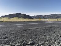 a yellow sign sitting on the side of a road next to a dirt field and mountains