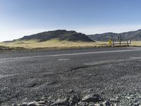 a yellow sign sitting on the side of a road next to a dirt field and mountains