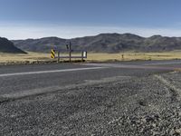 a yellow sign sitting on the side of a road next to a dirt field and mountains