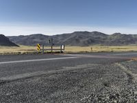 a yellow sign sitting on the side of a road next to a dirt field and mountains