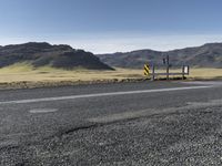 a yellow sign sitting on the side of a road next to a dirt field and mountains