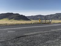 a yellow sign sitting on the side of a road next to a dirt field and mountains