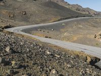 a man riding a motorcycle down the side of a desert road next to a mountain