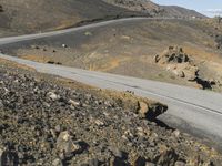 a man riding a motorcycle down the side of a desert road next to a mountain