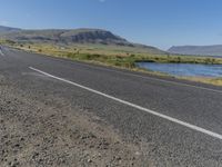 a motorcycle rides down the road in front of a mountain landscape in iceland with a river running through the valley