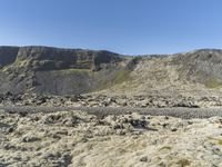 a group of people stand in an open field on the side of the mountain with grass and rocks all around