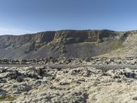 a group of people stand in an open field on the side of the mountain with grass and rocks all around