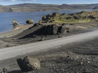 an automobile drives down the side of a winding road near the water and rocks, and a blue sky is in the background