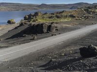 an automobile drives down the side of a winding road near the water and rocks, and a blue sky is in the background