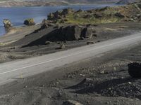 an automobile drives down the side of a winding road near the water and rocks, and a blue sky is in the background