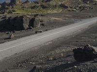 an automobile drives down the side of a winding road near the water and rocks, and a blue sky is in the background