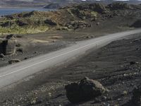 an automobile drives down the side of a winding road near the water and rocks, and a blue sky is in the background