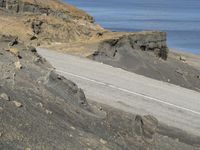 an aerial view of a person riding their motorcycle down a mountain road next to the ocean