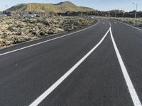 a white line on a road and a mountain in the background with some vegetation around it