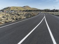 a white line on a road and a mountain in the background with some vegetation around it