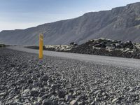 the road is made of pebbles, and there are mountains behind it and a yellow sign on either side