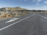 a desert road with an arrow painted on it in the distance is a large mountain with a village in the distance