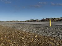 road sign in foreground of barren rocky terrain area under blue sky with clouds overhead