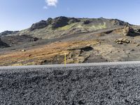 road going through black barren landscape on sunny day with a blue sky and mountain in the background