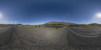 a fisheye view of a road leading to a lake and mountains with the sun on its side