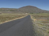 a long and narrow road leads through a dry landscape and mountains in the distance is hills with grass