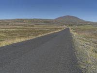 a long and narrow road leads through a dry landscape and mountains in the distance is hills with grass