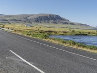 a long stretch of highway next to a mountain range by water, grass and bushes