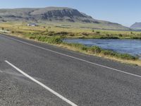 a long stretch of highway next to a mountain range by water, grass and bushes