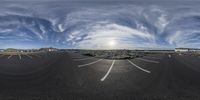 a road and a parking lot are seen in this fisheye photo, showing the sky and clouds