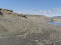 a rock cliff with lake in the back ground and mountains in the distance, in front of blue sky with clouds