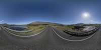 a long curved road runs past a grassy field with a stream running along it near a mountain