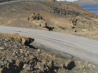 a motorcycle rider riding down the winding road with the ocean in the background a cliff