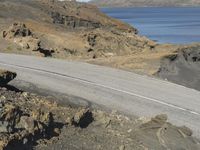 a motorcycle rider riding down the winding road with the ocean in the background a cliff