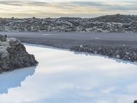 a person walking along a rocky hill beside some blue water and a rock formation with a reflection in it